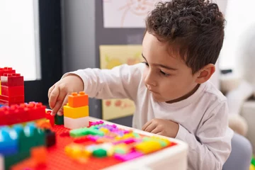 Fotobehang Lego Adorable hispanic boy playing with construction blocks sitting on table at kindergarten  © Krakenimages.com