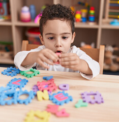 Adorable hispanic boy playing with vocabulary puzzle game sitting on table at kindergarten