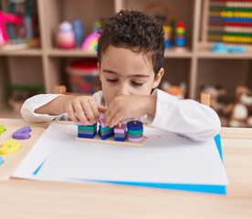 Adorable hispanic boy playing with toys sitting on table at kindergarten