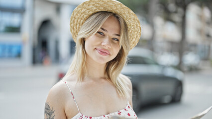 Young blonde woman tourist wearing summer hat smiling at street