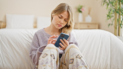 Young blonde woman using smartphone sitting on floor at bedroom