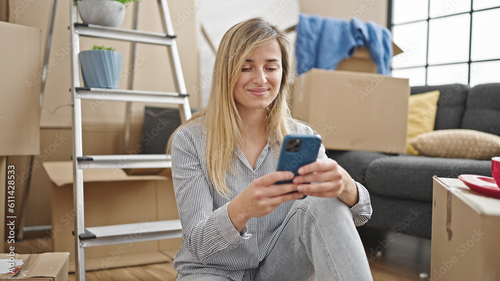 Sticker young blonde woman using smartphone sitting on floor at new home