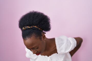 African woman with curly hair standing over pink background suffering of backache, touching back with hand, muscular pain