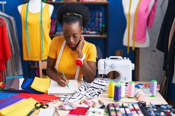 African american woman tailor writing on notebook at sewing studio