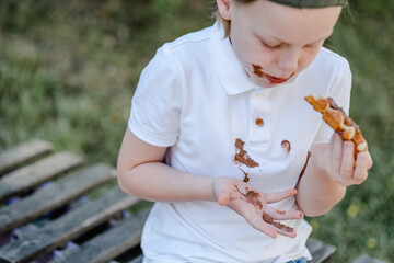 A child showing a melting chocolate on his hand. Dirty chocolate stains on white clothes