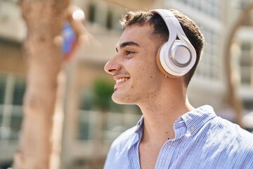 Young hispanic man smiling confident listening to music at street