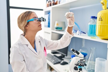 Young hispanic woman scientist looking diamond with zoom glasses at laboratory