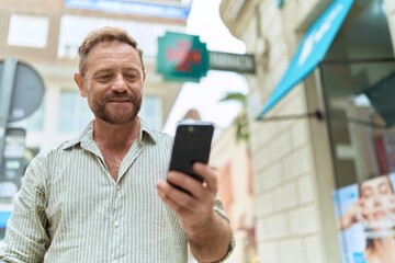 Obraz na płótnie Canvas Middle age man smiling confident using smartphone at pharmacy