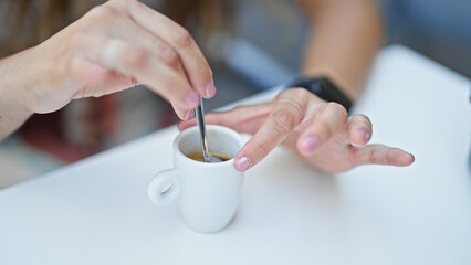 Young beautiful hispanic woman sitting on table stir the coffee at coffee shop terrace