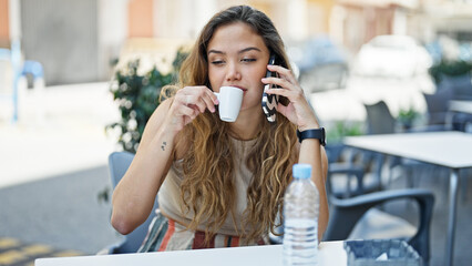 Young beautiful hispanic woman talking on the smartphone drinking coffee at coffee shop terrace