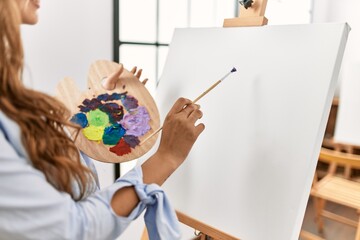 Young beautiful hispanic woman artist drawing on back view at art studio