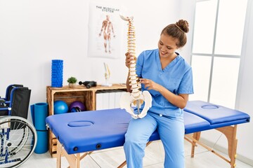 Young beautiful hispanic woman physiotherapist smiling confident holding anatomical model of spinal...