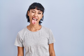 Young hispanic woman wearing casual t shirt over blue background sticking tongue out happy with funny expression. emotion concept. © Krakenimages.com