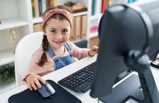 Adorable hispanic girl student using computer sitting on table at classroom