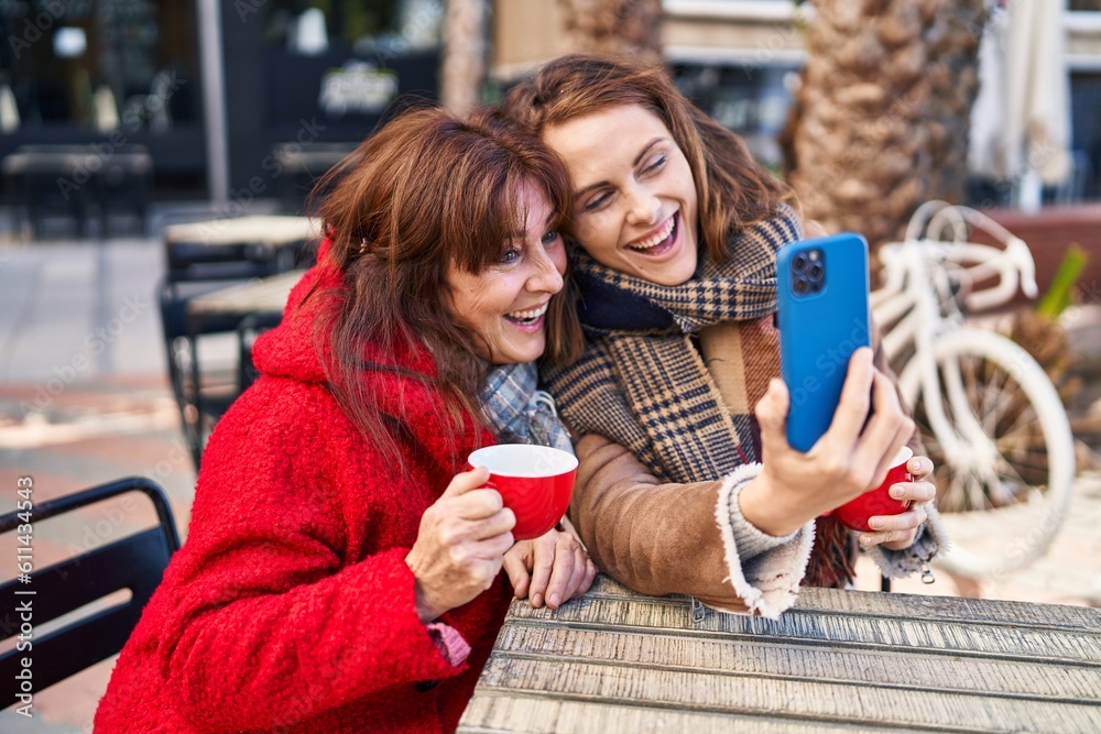 Wall mural Two women mother and daughter using smartphone drinking coffee at coffee shop terrace