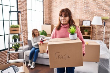 Mother and daughter moving to a new home holding cardboard box skeptic and nervous, frowning upset because of problem. negative person.