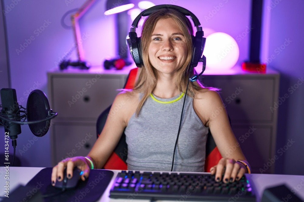 Poster blonde caucasian woman playing video games with headphones looking positive and happy standing and s