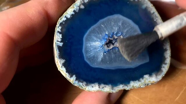A caucasian man cleaning a blue agate mineral with a brush.