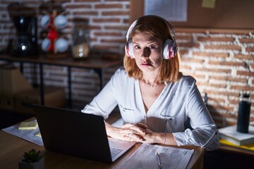 Young redhead woman working at the office at night wearing headphones depressed and worry for distress, crying angry and afraid. sad expression.