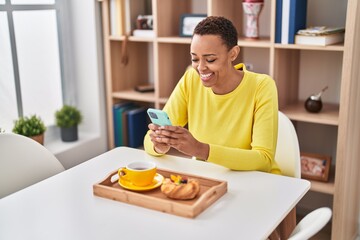 African american woman having breakfast using smartphone at home
