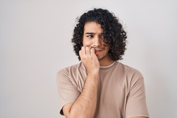 Fototapeta na wymiar Hispanic man with curly hair standing over white background looking stressed and nervous with hands on mouth biting nails. anxiety problem.