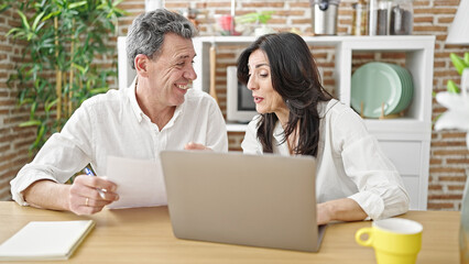 Senior man and woman couple using laptop reading document at dinning room