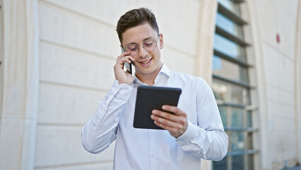 Young hispanic man talking on smartphone using touchpad at hospital