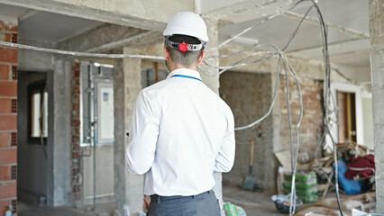 Young hispanic man architect standing backwards at construction site
