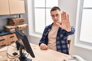 Young hispanic man ecommerce business worker doing stop gesture with hand at office