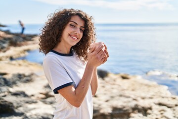 Young hispanic woman smiling confident drinking coffee at seaside