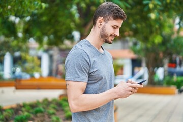 Naklejka na ściany i meble Young caucasian man smiling confident using smartphone at park
