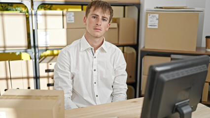 Young caucasian man ecommerce business worker sitting on table with relaxed expression at office