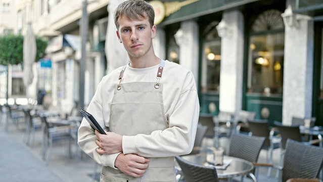 Young caucasian man waiter smiling confident using touchpad at coffee shop terrace