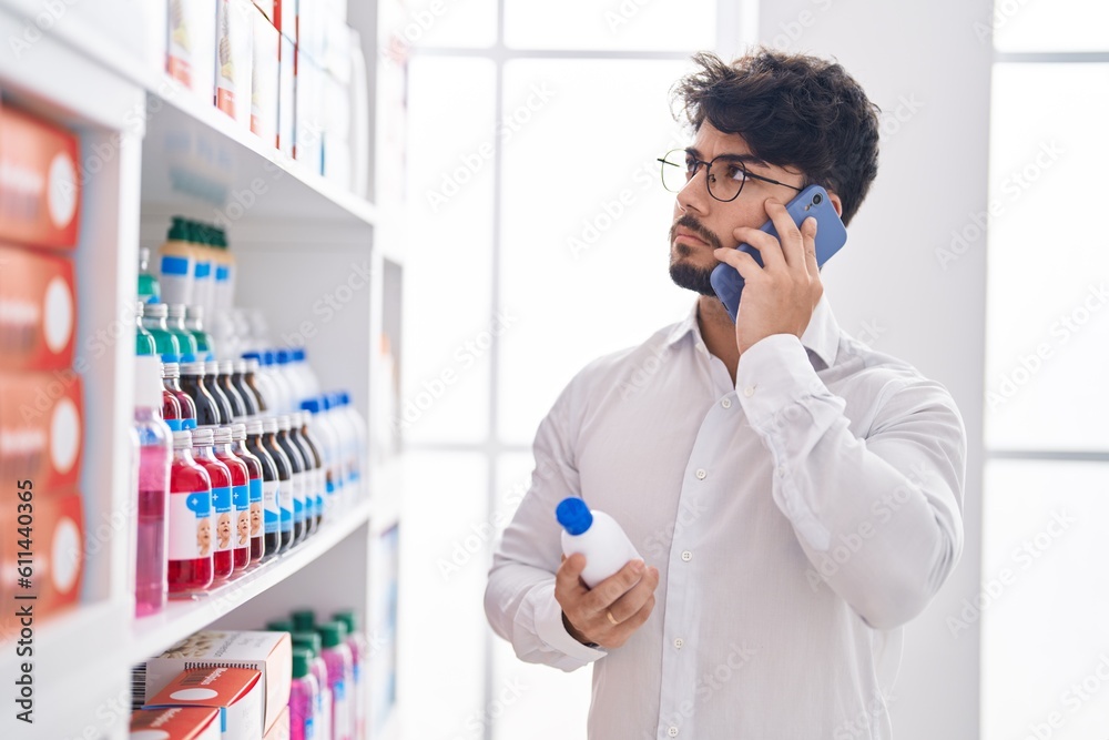 Sticker young hispanic man client talking on smartphone holding bottle at pharmacy