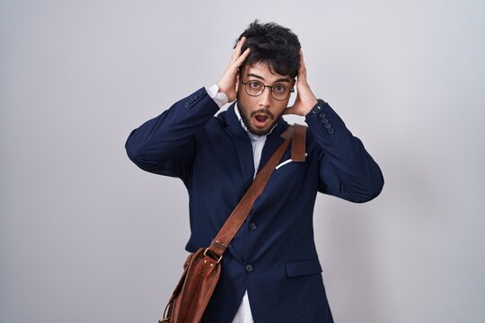 Hispanic man with beard wearing business clothes crazy and scared with hands on head, afraid and surprised of shock with open mouth