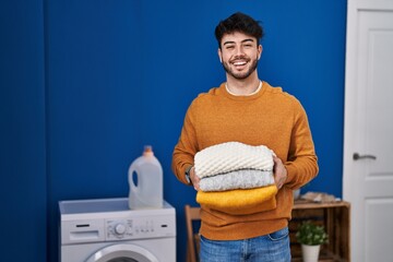 Hispanic man with beard holding clean folded laundry celebrating crazy and amazed for success with...