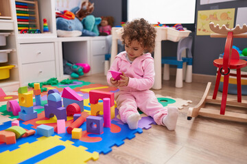 Adorable hispanic girl playing with construction blocks sitting on floor at kindergarten
