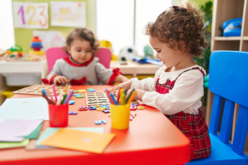 Adorable girls playing with maths puzzle game sitting on table at kindergarten