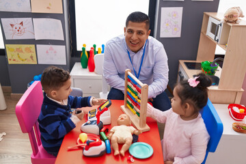 Hispanic man with boy and girl playing with abacus sitting on table at kindergarten