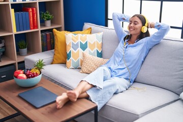 Young beautiful hispanic woman listening to music relaxed on sofa at home