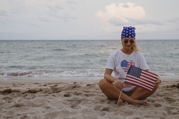 The girl is sitting on the beach with the American flag. Patriotism. Girl on the beach. Independence Day