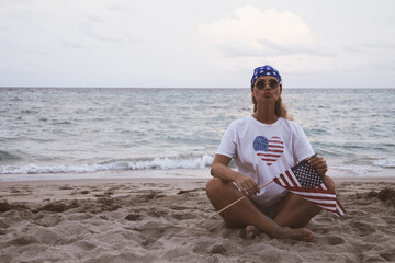 The girl is sitting on the beach with the American flag. Patriotism. Girl on the beach. Independence Day