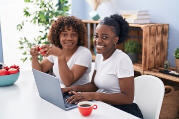 African american women mother and daughter drinking coffee using laptop at home