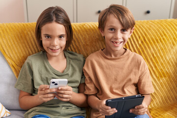 Adorable boys using smartphone and touchpad sitting on sofa at home