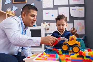 Hispanic man and boy playing with construction blocks and tractor toy at kindergarten