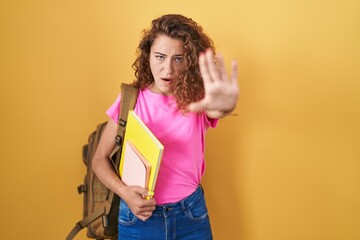 Young caucasian woman wearing student backpack and holding books doing stop gesture with hands palms, angry and frustration expression