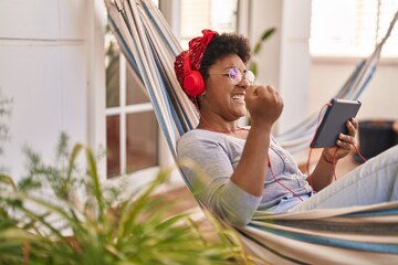 African american woman watching movie on touchpad lying on hammock at home terrace