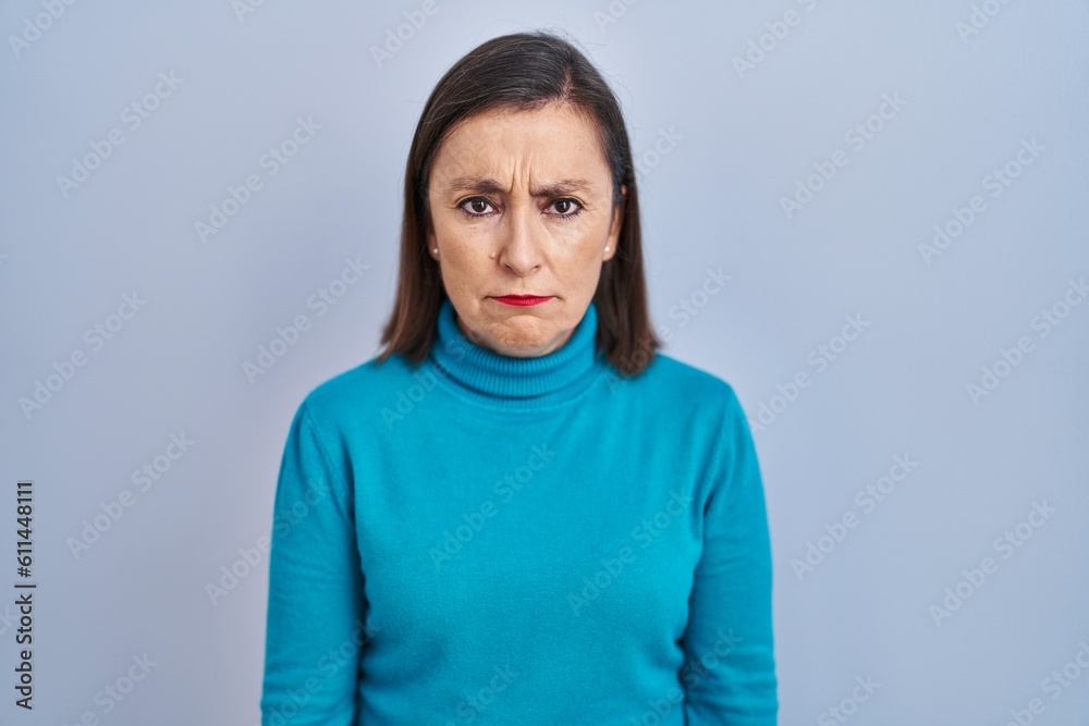 Wall mural middle age hispanic woman standing over isolated background skeptic and nervous, frowning upset beca