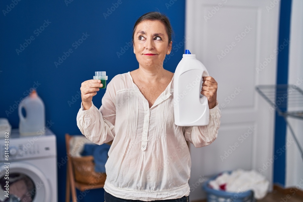 Wall mural middle age hispanic woman holding detergent bottle smiling looking to the side and staring away thin