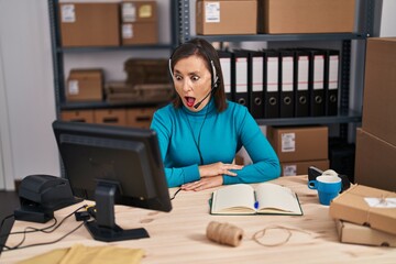 Middle age hispanic woman working at small business ecommerce on customer support scared and amazed with open mouth for surprise, disbelief face